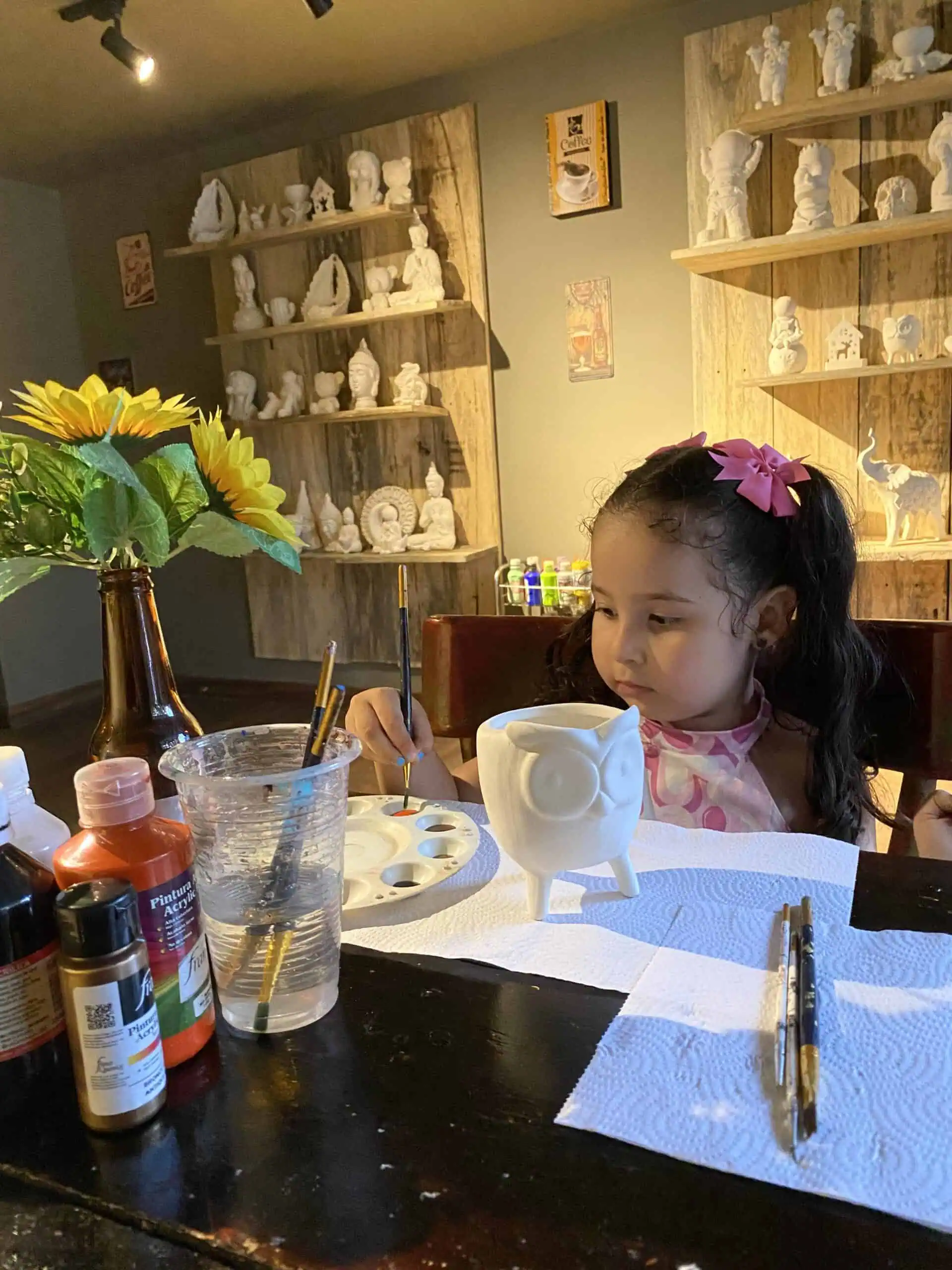 在一个充满乐趣的活动中，孩子们正在艺术桌上绘制白色陶瓷，背景装饰着鲜花和人物，旨在促进创造力和家庭娱乐。