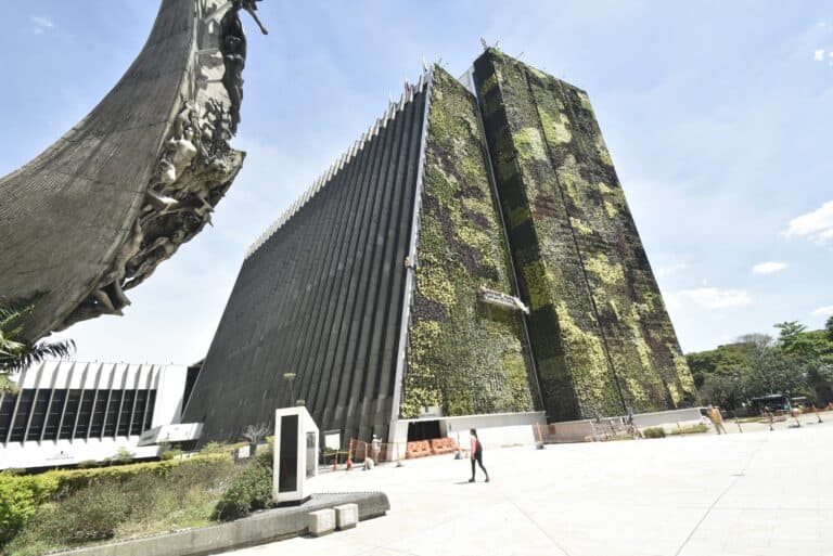 Edificio moderno con fachada verde de plantas y escultura artística en un espacio público en Bogotá, Colombia.