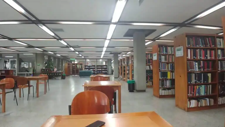 Une bibliothèque moderne avec des étagères remplies de livres, des tables d'étude et un éclairage fluorescent, idéale pour les événements, les études et la lecture dans un environnement calme et académique.