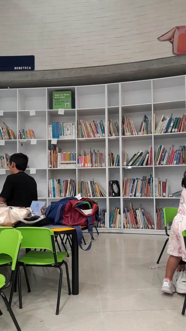 Biblioteca pública con estanterías llenas de libros y espacio de estudio para eventos culturales y educativos.