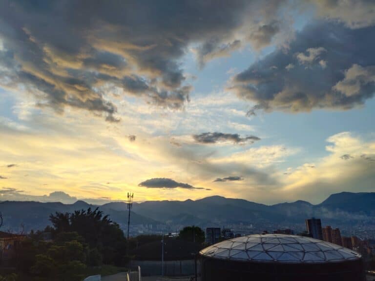 Nubes y cielo al atardecer en un paisaje urbano con montañas de fondo.