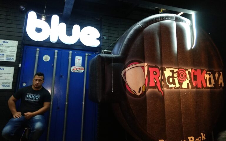 Blue, logotipo de evento y ambiente de bar, con una persona sentada y elementos decorativos en un establecimiento nocturno en Bogotá.