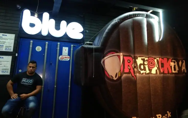 蓝色、活动标志和酒吧氛围，画面中有一个人坐在波哥大的一家夜总会里，周围还有一些装饰元素。