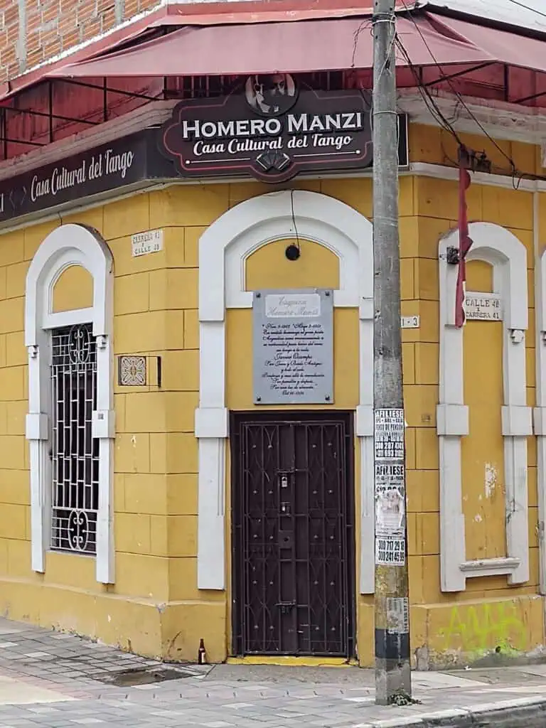 霍梅罗·曼齐探戈文化中心是一栋黄色建筑，窗户装有铁栅栏，入口处挂着一块荣誉标志，位于哥伦比亚波哥大的一条城市街道上。
