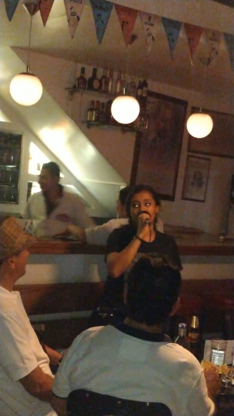 Eventario.co imagen de evento en bar con personas disfrutando y cantante en vivo, ambiente festivo, decoración con banderines y iluminación cálida, ideal para organizar eventos y celebraciones.