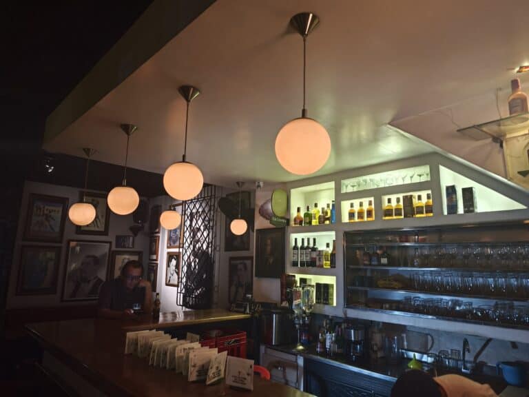 Bar de restaurante con iluminación cálida, exhibición de botellas de licor y ambiente acogedor decorado con retratos en las paredes.