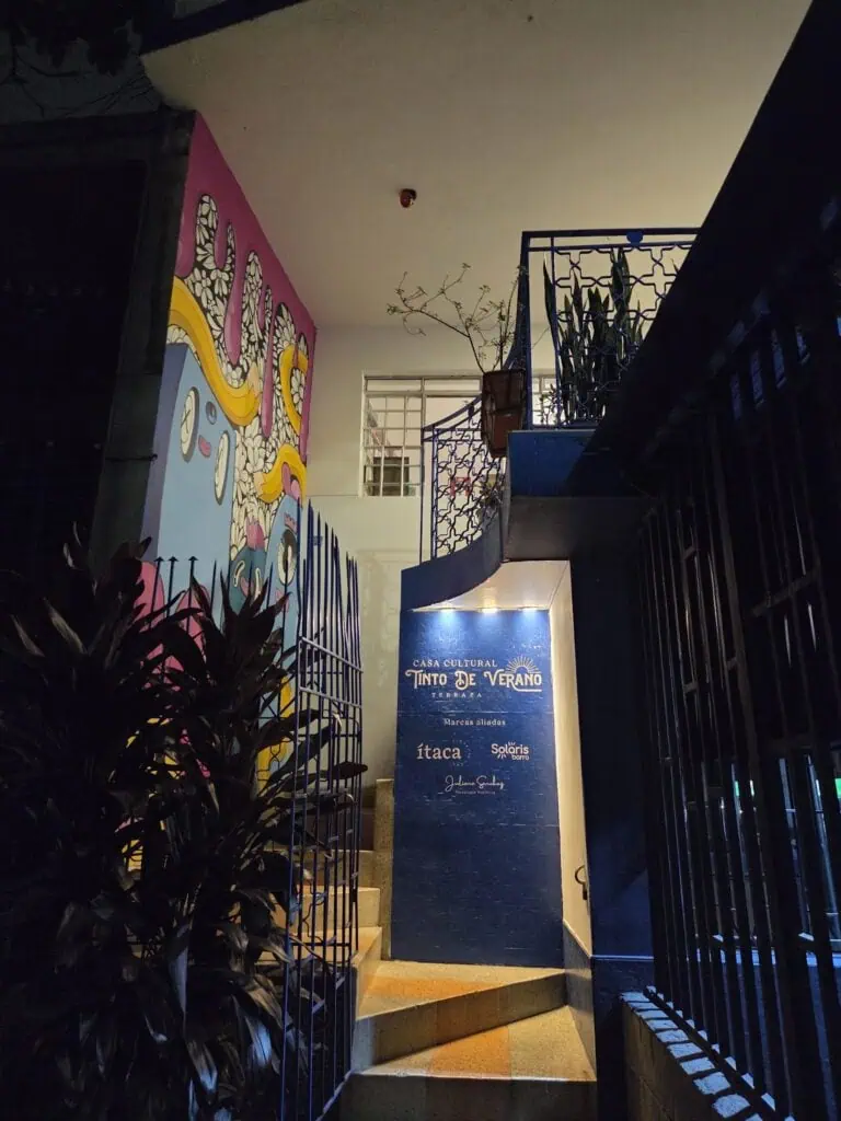 Accès à la Casa Culture Tinto de Verano sur la terrasse avec des mosaïques colorées, une signalétique de marques partenaires et une ambiance nocturne, idéale pour des événements culturels et sociaux dans des espaces ouverts et modernes.