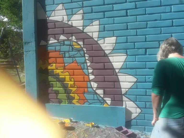 Colorido mural de graffiti en una pared de ladrillos, con un artista pintando un diseño innovador y creativo en un espacio al aire libre.