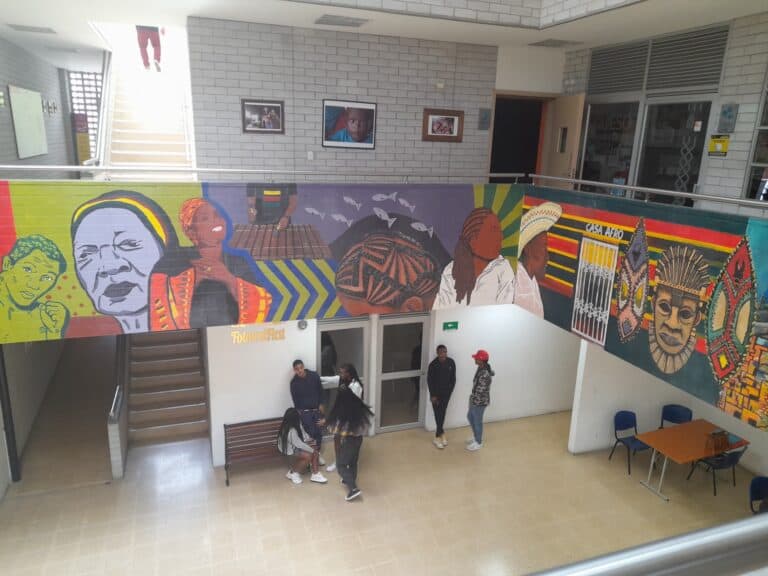 Colorido mural de arte urbano en un espacio interior, con figuras culturales, símbolos africanos y personajes tradicionales, en un ambiente universitario o de eventos culturales.