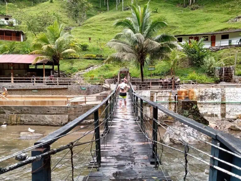 Ponte di legno sopra una sorgente termale in una spa naturale circondata da palme e natura in Colombia, ideale per eventi e viaggi avventurosi.