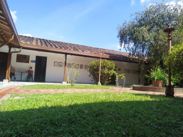 Fachada de un edificio con jardín y césped, estructura de techos de teja y paredes blancas, utilizado para eventos y reuniones, en un entorno natural y tranquilo en Colombia.