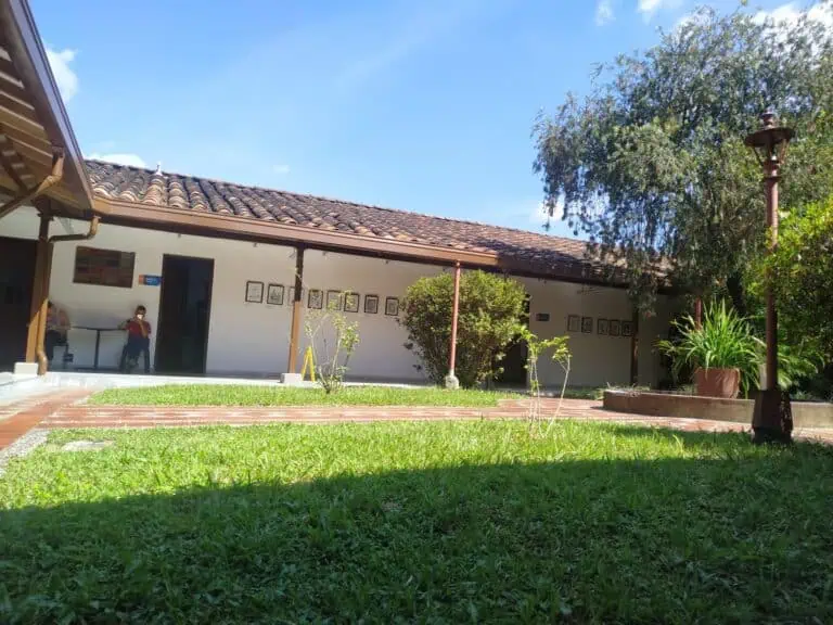 Façade d'un bâtiment avec jardin et pelouse, structure de toit en tuiles et murs blancs, utilisé pour des événements et des réunions, dans un cadre naturel et tranquille en Colombie.