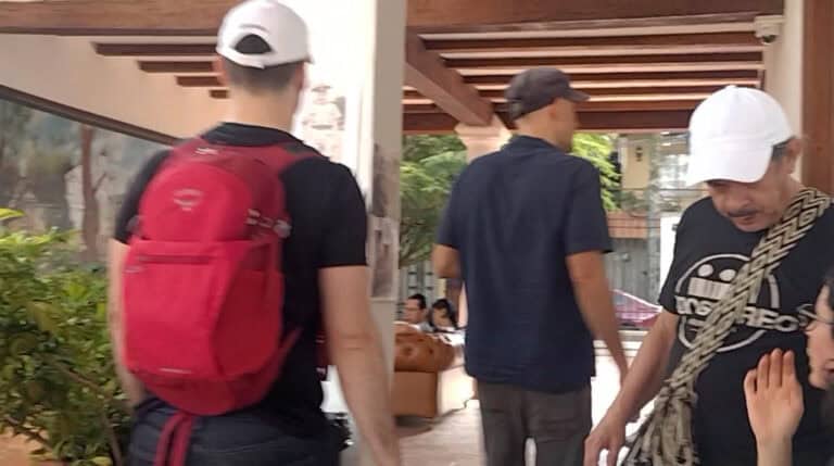 Personas en un evento social en un espacio cubierto, interactuando y socializando, con mochilas y vestimenta casual, en un ambiente amigable y dinámico.