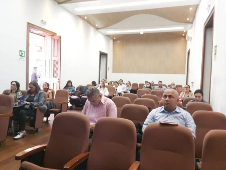 Asistentes en auditorio durante conferencia o seminario en evento empresarial en un espacio cerrado. Personas sentadas en sillas de auditorio, participando en una jornada de capacitación, networking o reunión corporativa.