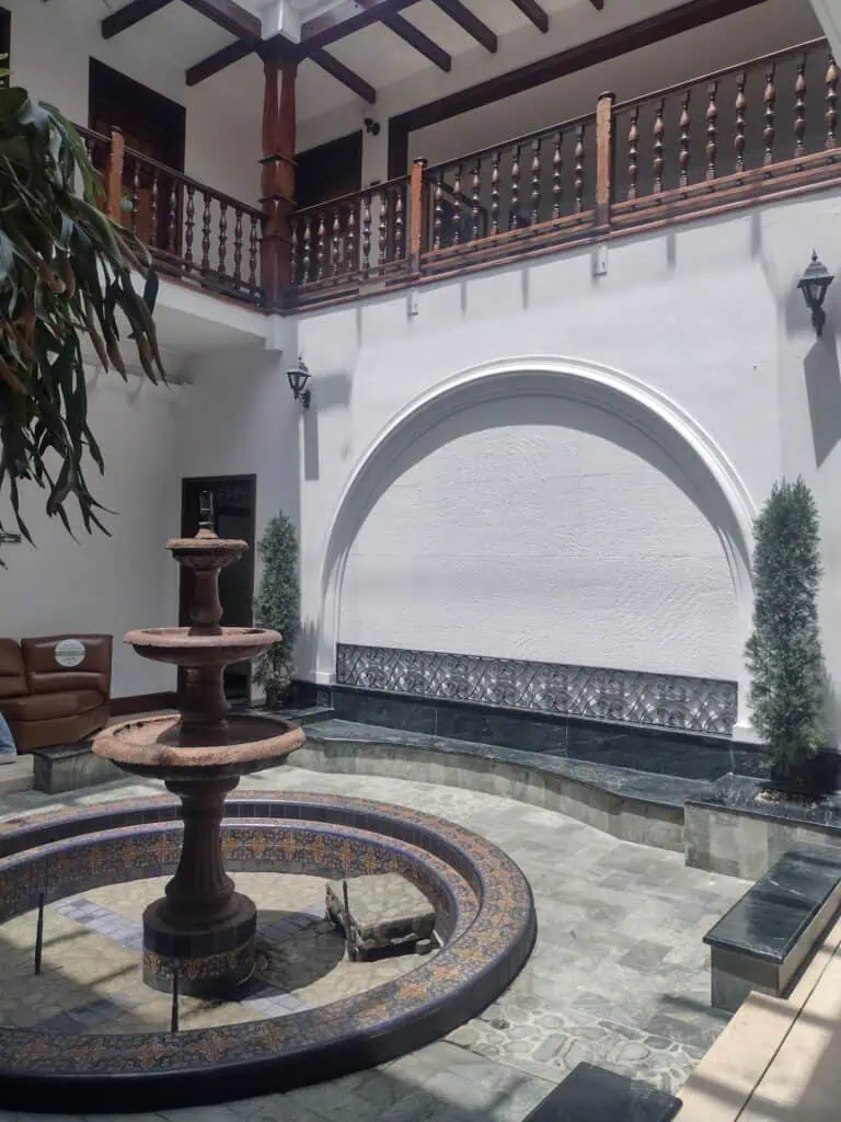 庭院内摆放着装饰花瓶，周围环绕着水景和盆栽植物。这栋殖民风格的房屋拥有优雅宜人的空间，配有木质阳台和白色墙壁，是举办活动和聚会的理想场所。