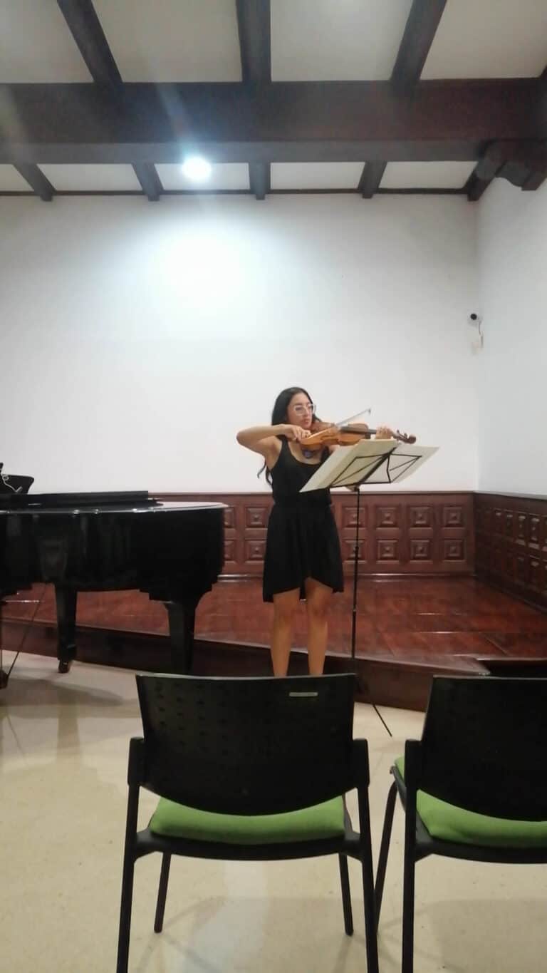 Afinador de violín en concierto en un espacio interior con piano y asientos.