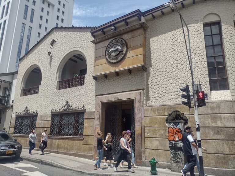 Amplia fachada de edificio histórico con letrero de "POETEA" y detalles arquitectónicos clásicos en la ciudad, en medio del movimiento urbano y peatones en la acera.