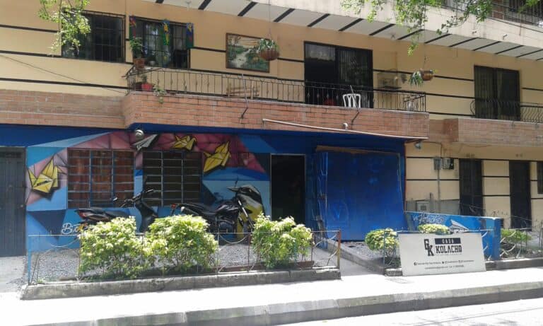 住宅楼内一家商店的外墙上绘有色彩鲜艳的壁画，公共道路上停放着摩托车，还有一个宣传标牌。