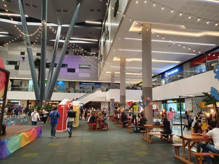 Colorido centro comercial con espacios de ocio y comida, ambiente moderno, iluminación ambiental, y áreas para eventos y reuniones en un espacio abierto y concurrido.