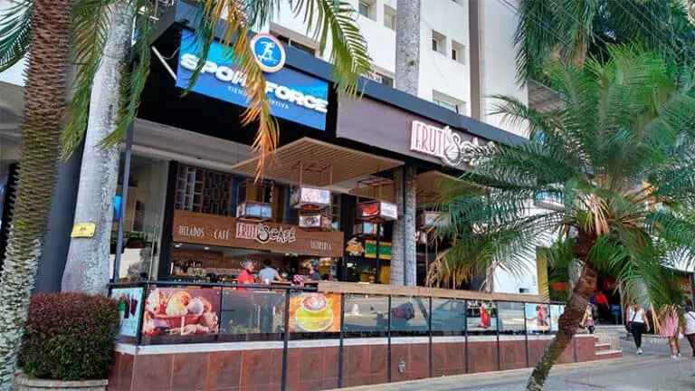 Photo d'archives d'un café et glacier appelé Fruit Café dans une rue piétonne bordée de palmiers et de passants, idéale pour promouvoir des événements, de la nourriture et des restaurants lors d'événements en Colombie.