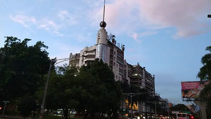 Modern building in an urban area of ​​a Colombian city at sunset, with trees and vehicular traffic.