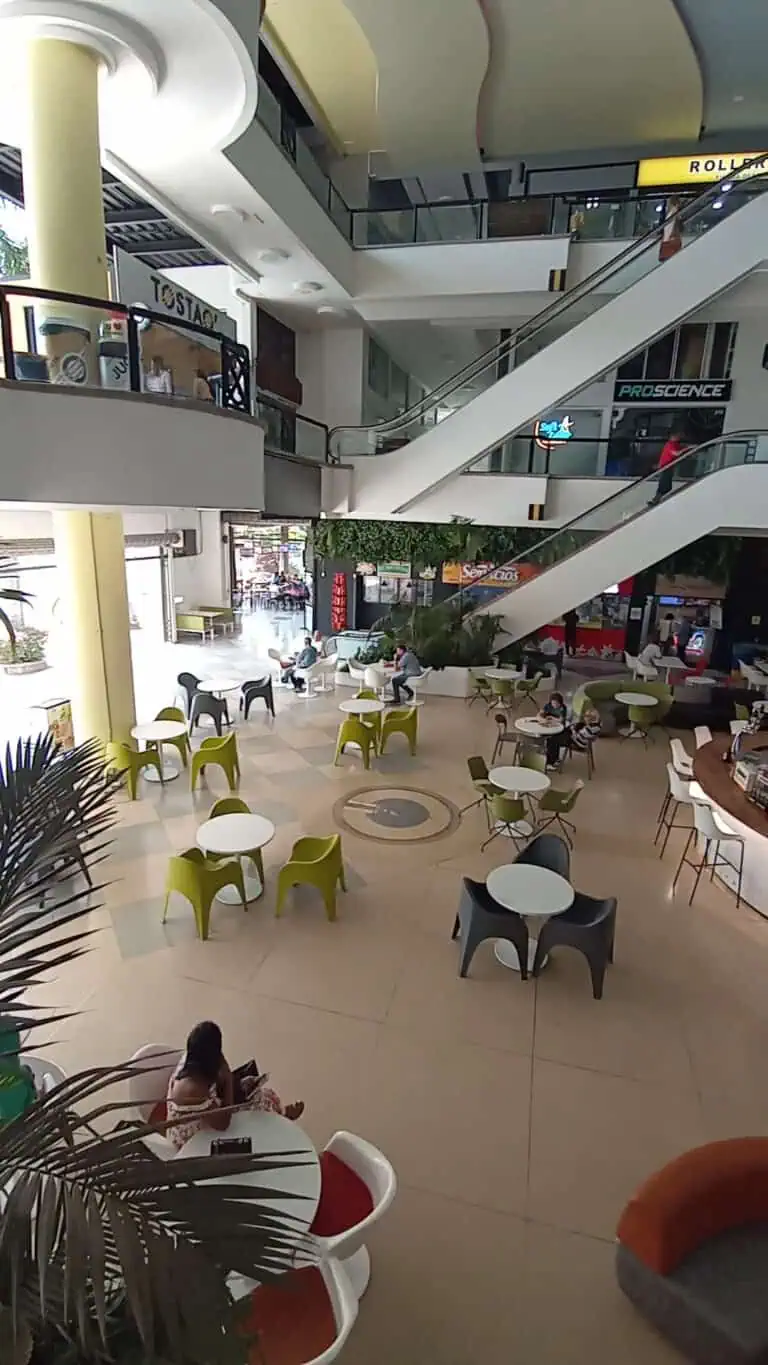 Eventario Shopping center in a food and rest area, with modern tables and chairs, escalators, and a lively atmosphere inside a mall in Colombia.