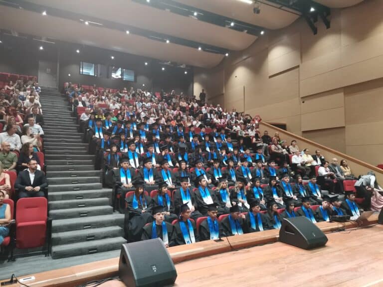 Estudiantes graduados en toga y birrete en ceremonia académica en auditorio moderno.