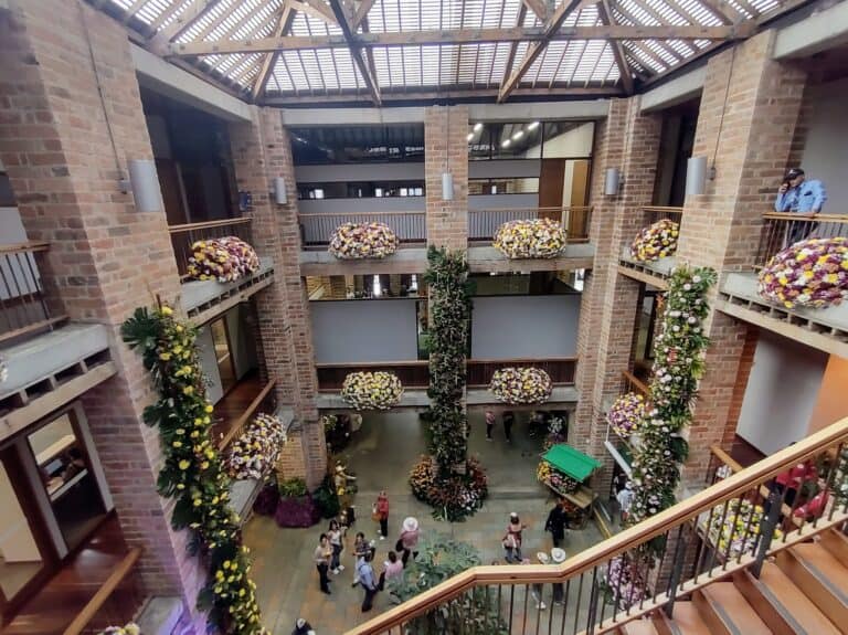 Esquina interior de edificio de eventos con decoración floral en los balcones y columnas, resaltando la organización y elegancia para eventos sociales y empresariales en un entorno moderno y acogedor.