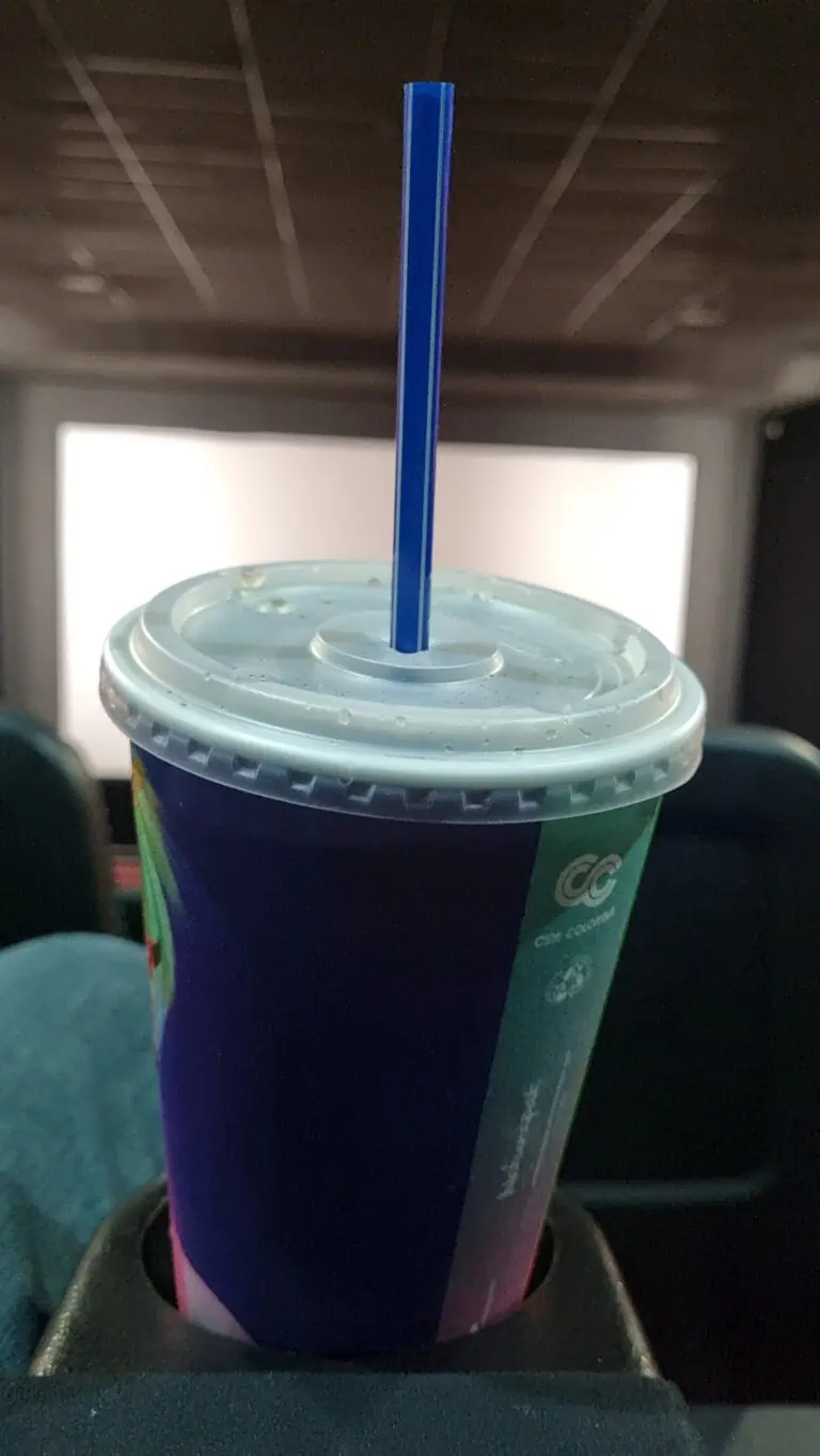 清爽的饮料装在带盖的杯子里，配有蓝色吸管，从电影院内部拍摄，背景是屏幕，非常适合活动和娱乐。