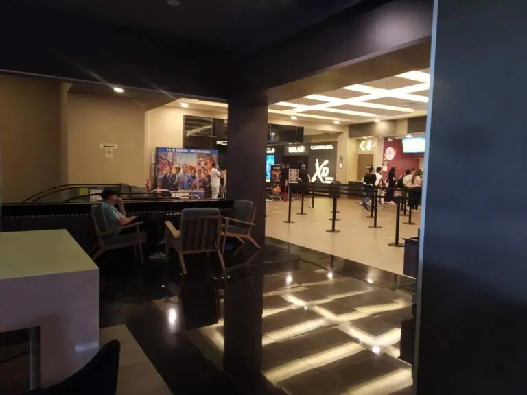 Entrée d'une salle de cinéma dans un centre commercial, avec des gens faisant la queue, des panneaux d'affichage et des zones d'attente, représentant des services d'événements et de divertissement.