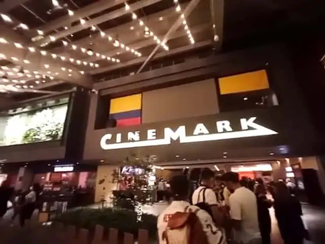 Ein Kino in einem Einkaufszentrum mit dekorativer Beleuchtung und Beschilderung, einer geschäftigen Atmosphäre und Besuchern, die den Raum und den Film genießen.