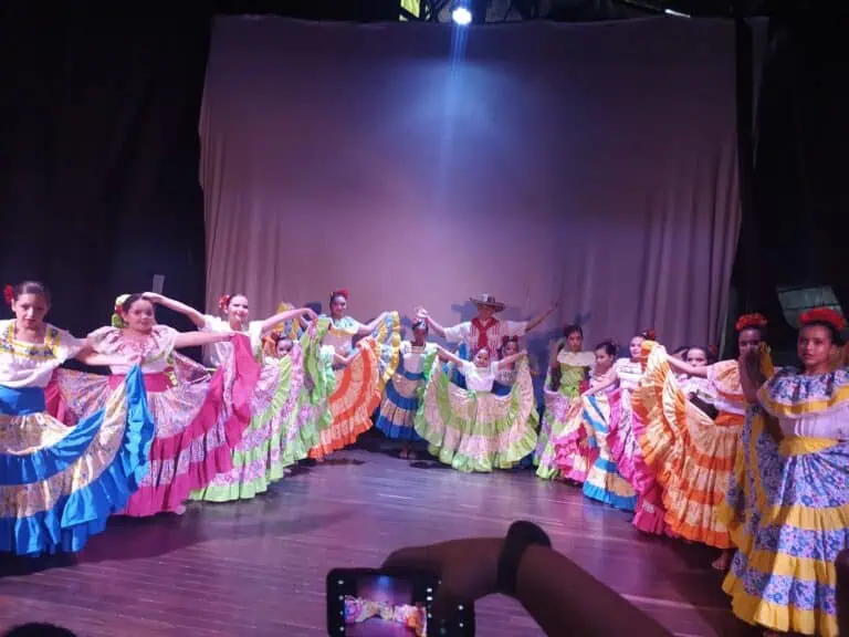 Des danseurs enfants exécutent une performance culturelle en costumes traditionnels mexicains, chorégraphiés sur scène avec un décor en toile de fond.