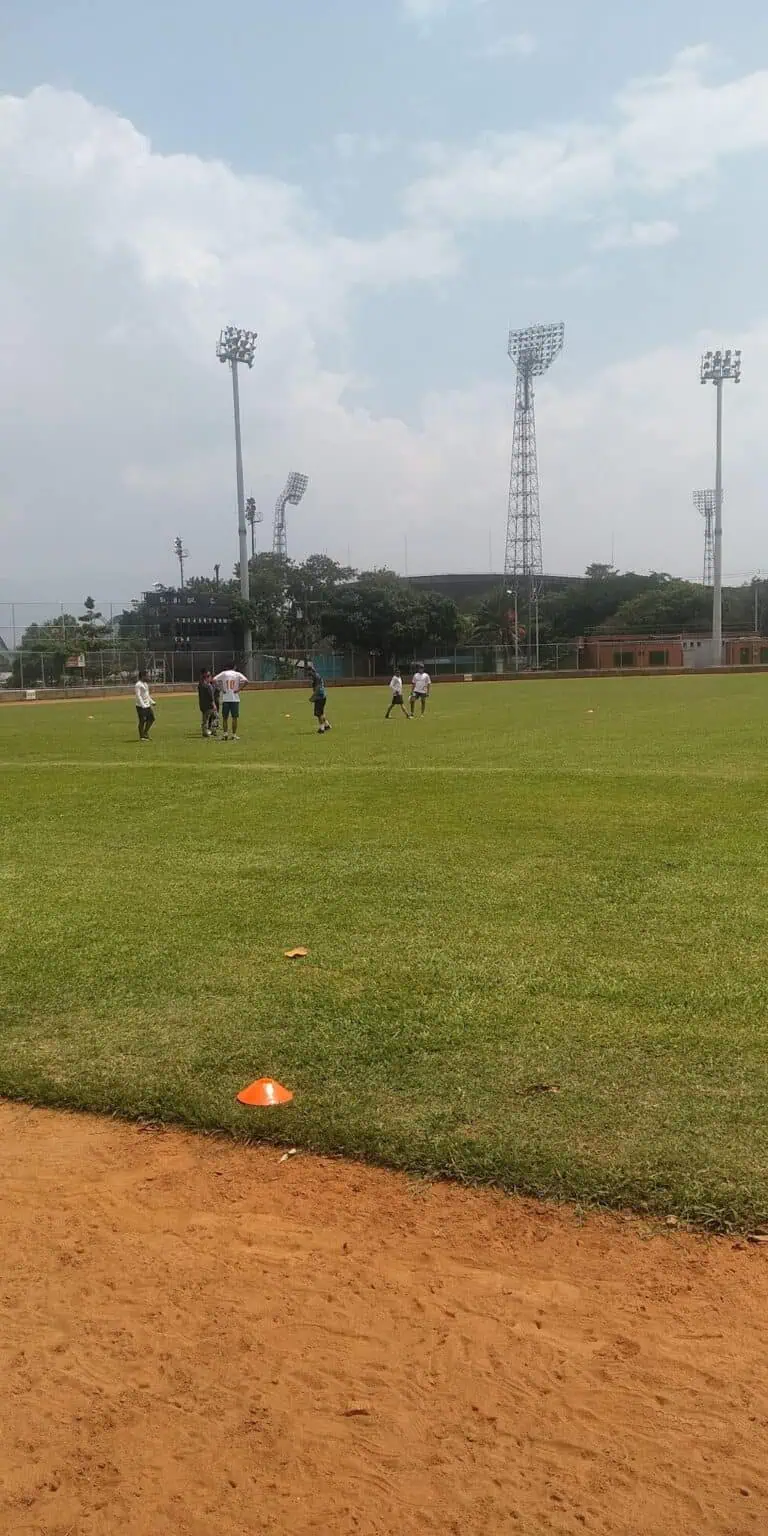 户外足球训练，球员们在维护良好的大草坪上练习，背景是泛光灯和体育场，天空阴云密布。