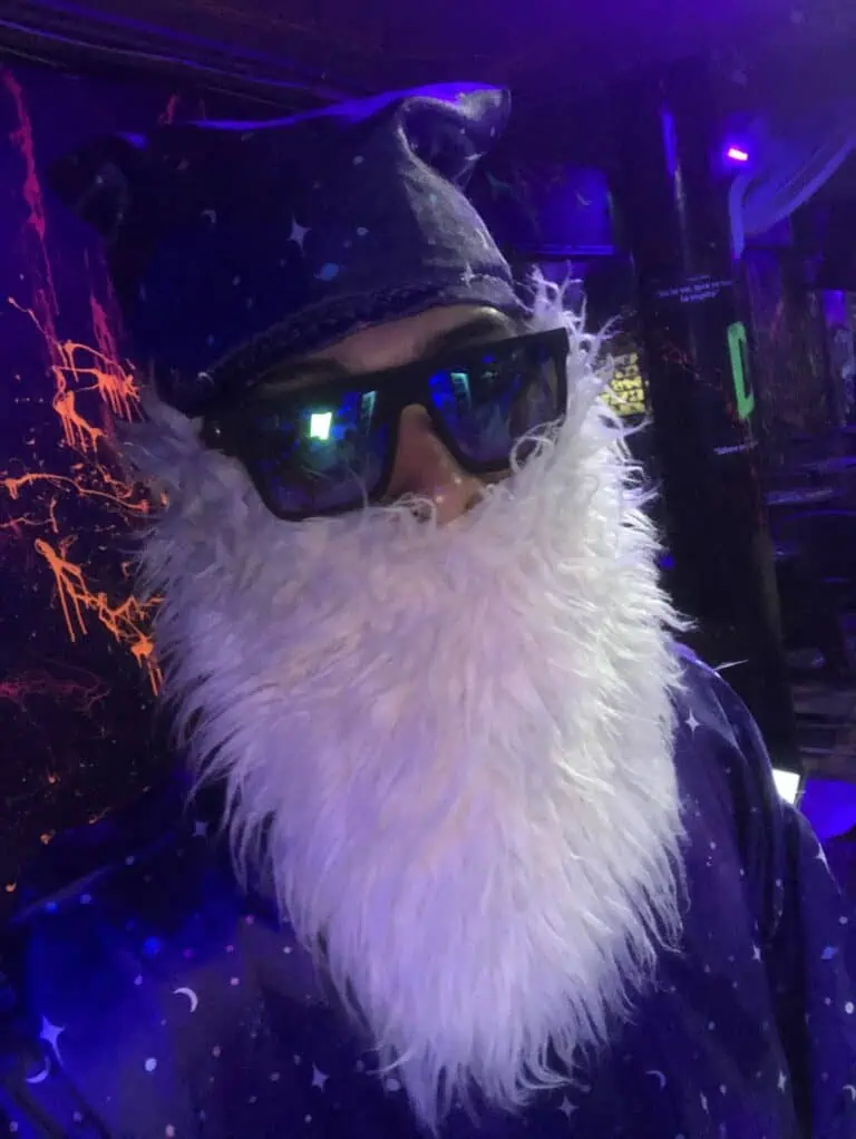 Santa Claus costume with a white beard, hat, and dark glasses in a nighttime setting with ultraviolet lights, perfect for Christmas-themed events and festive celebrations.