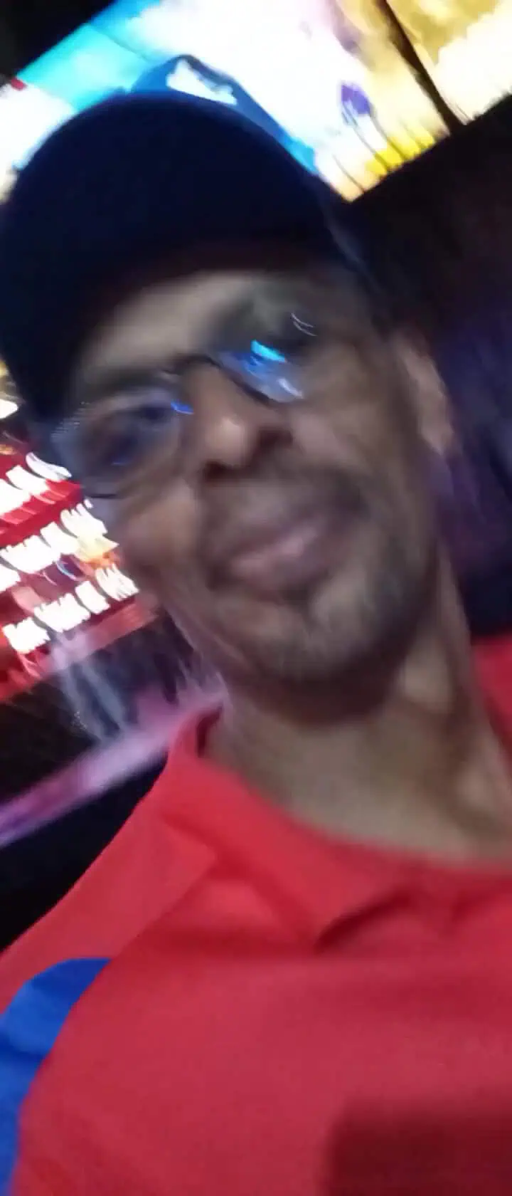Eventario, image of a man wearing glasses and a cap at a night event in Colombia, background of neon lights and screens, event, technology, entertainment, social gathering.