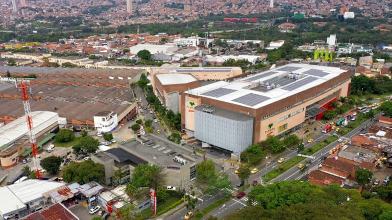 Centro comercial y área urbana de Bogotá vista aérea, con edificios modernos, calles transitadas y zonas verdes en un día soleado.