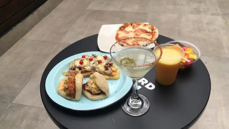 Une délicieuse variété de plats et de boissons lors d'un événement social, notamment des pizzas, des sandwichs, des cocktails et des jus naturels dans une atmosphère décontractée.