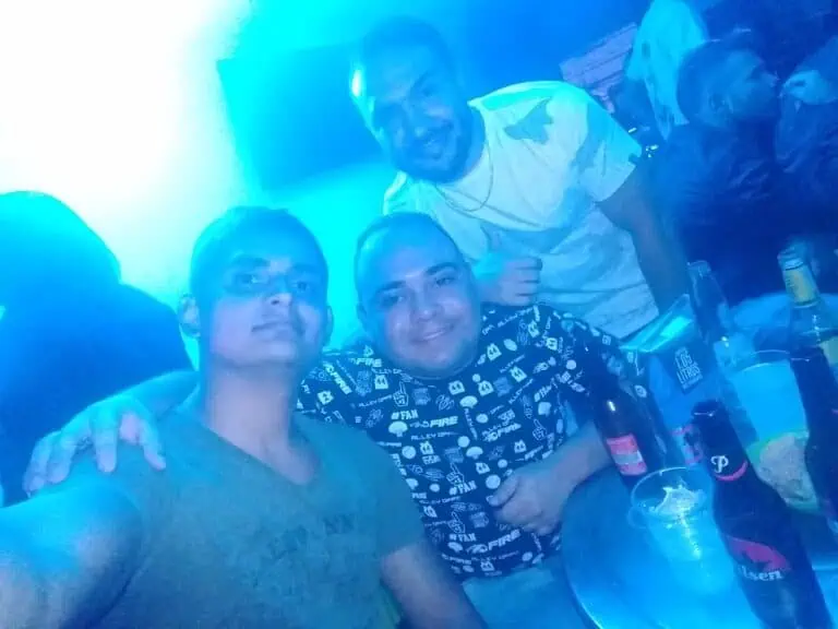 Personas disfrutando de un evento social en un ambiente con iluminaci&oacute;n azul, con bebidas en la mesa, en un ambiente festivo y de camarader&iacute;a, promoviendo la organizaci&oacute;n de eventos y networking.
