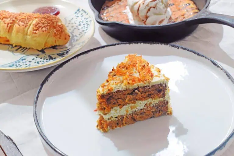 一块美味的胡萝卜蛋糕，上面涂着奶油奶酪糖霜，放在白色盘子上，桌上还摆放着几种甜点选择。