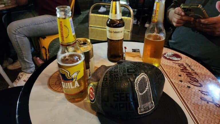 Botellas de cerveza y una gorra en una mesa de bar, ambiente nocturno, personas disfrutando de una salida social.