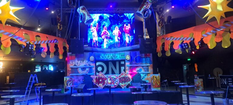 Luces y escenario de evento en un club nocturno con decoración colorida y música en vivo. Ambiente vibrante y moderno para fiestas y eventos culturales en Medellín, Colombia.
