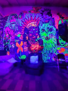 Vibrante mural de arte fluorescente con personajes y animales en neón, ideal para eventos y exposiciones creativas en espacios de arte moderno en Colombia.