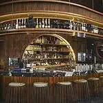 Elegant bar furniture in a restaurant with warm lighting, shelves with various liquor bottles, drinks, and glassware, a sophisticated ambiance for events and social gatherings.
