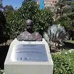 Buste du Mahatma Gandhi dans un parc avec végétation et bâtiments en arrière-plan, dédié à la promotion de la paix et de la non-violence.