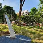 Chuta de resbaladilla de metal en parque infantil al aire libre, rodeada de árboles verdes y zonas de juego para niños en un entorno urbano.