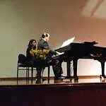 Singing student performing musicals, accompanied by a pianist on the stage of a cultural event, demonstrating talent and technique in vocal and piano performance in an artistic and professional environment.