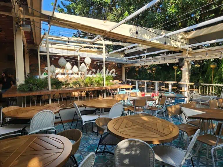 Terrasse de restaurant avec tables en bois, chaises variées, décor moderne et éclairage immersif, idéale pour les événements et réunions en plein air en pleine nature.