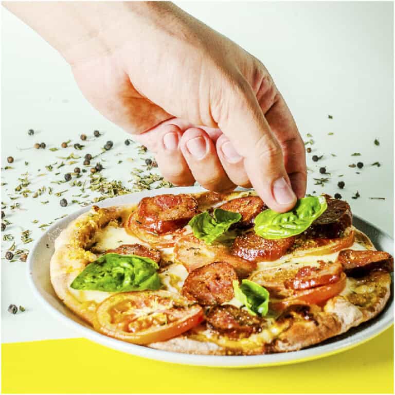 Disfruta de una deliciosa pizza con ingredientes frescos, con toppings de pepperoni, tomate y hojas de albahaca, perfecta para eventos y reuniones.