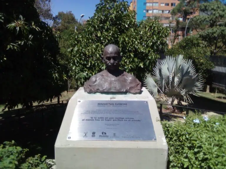 Un buste du Mahatma Gandhi dans un parc urbain avec une variété de plantes et de bâtiments urbains en arrière-plan, symbole de paix et de leadership dans l'indépendance, à Medellín, en Colombie.