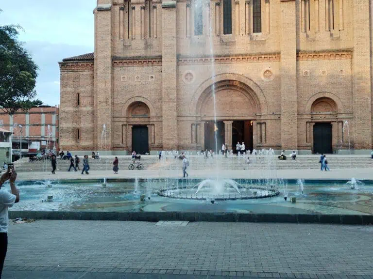 Die Kathedrale von Pasto, ein imposantes braunes Bauwerk, steht vor einem öffentlichen Brunnen im Stadtzentrum, ist von Menschen und kulturellen und religiösen Aktivitäten umgeben und symbolisiert die Geschichte und Kultur von Nariño.